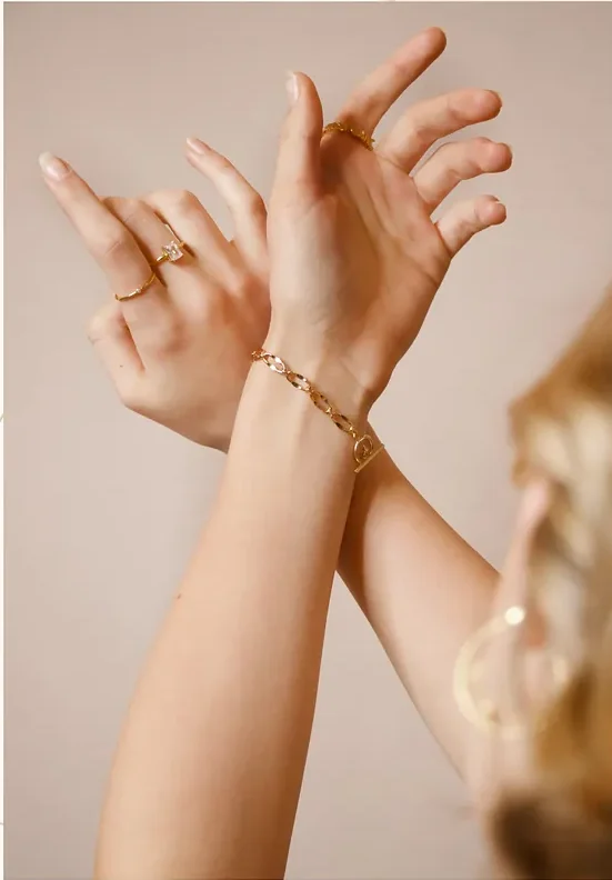 Two hands crossed at the wrist, wearing several gold bracelets and rings.